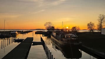 A calm waterway with boats docked at a pier, a clear sky, and a sunset.
