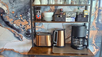 Une cuisine avec un dosseret en marbre, des appareils en acier inoxydable et une machine à café posée sur une étagère.
