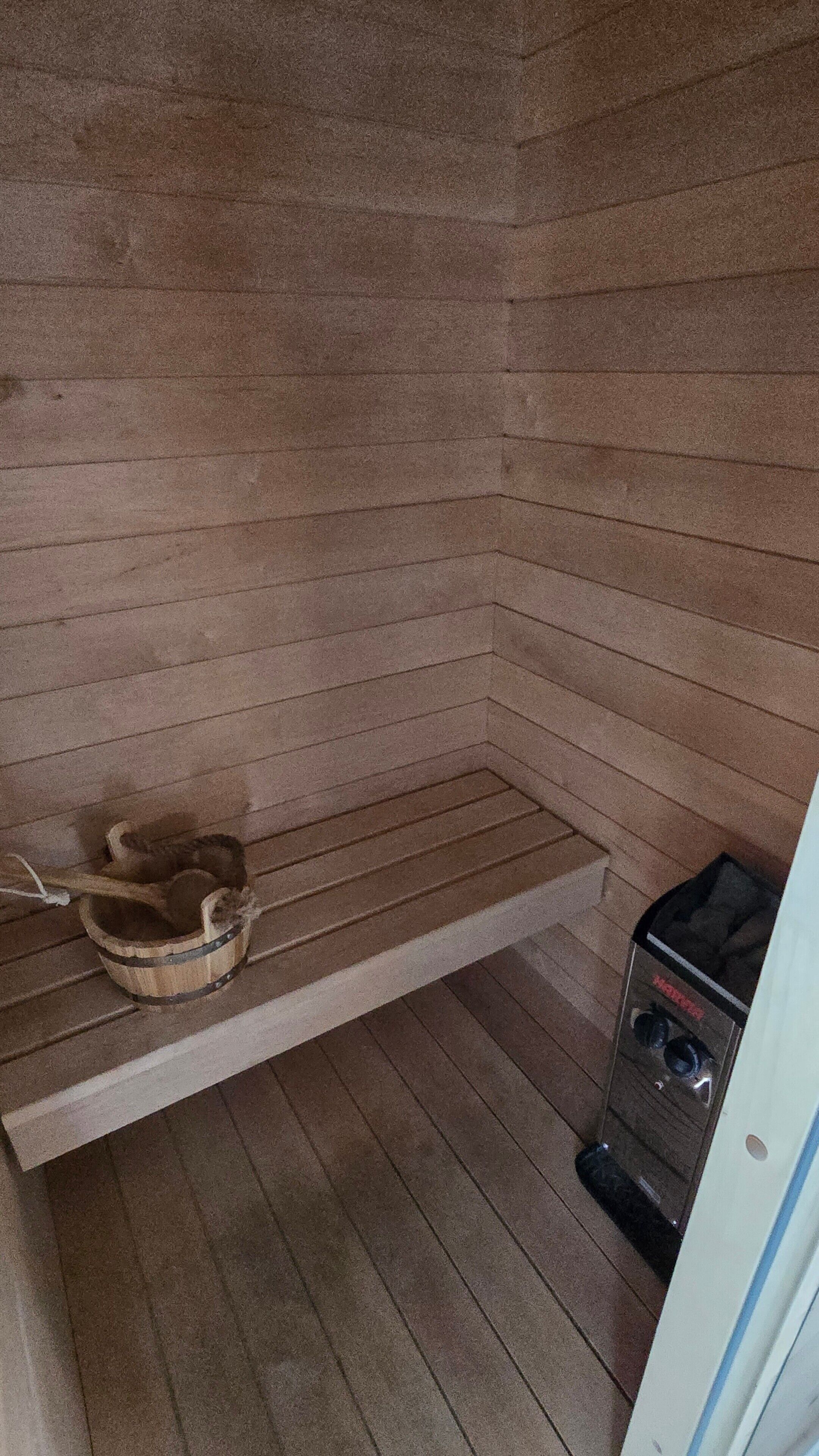 A sauna room with a wooden bench, a wooden bucket, and a sauna heater.
