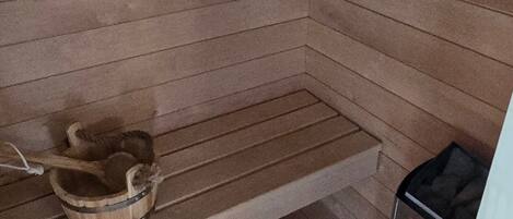 A sauna room with a wooden bench, a wooden bucket, and a sauna heater.
