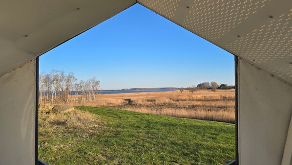 A view through a triangular window of a grassy field with a body of water in the distance.