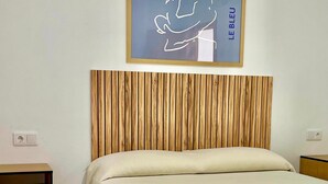 A bedroom with a wooden headboard, a bed with a floral bedspread, a nightstand, and a wall-mounted picture frame. - Casa Golondrinas Verdes, Cartaya – Private Garden, Beach & Pets Welcome (Cartaya)