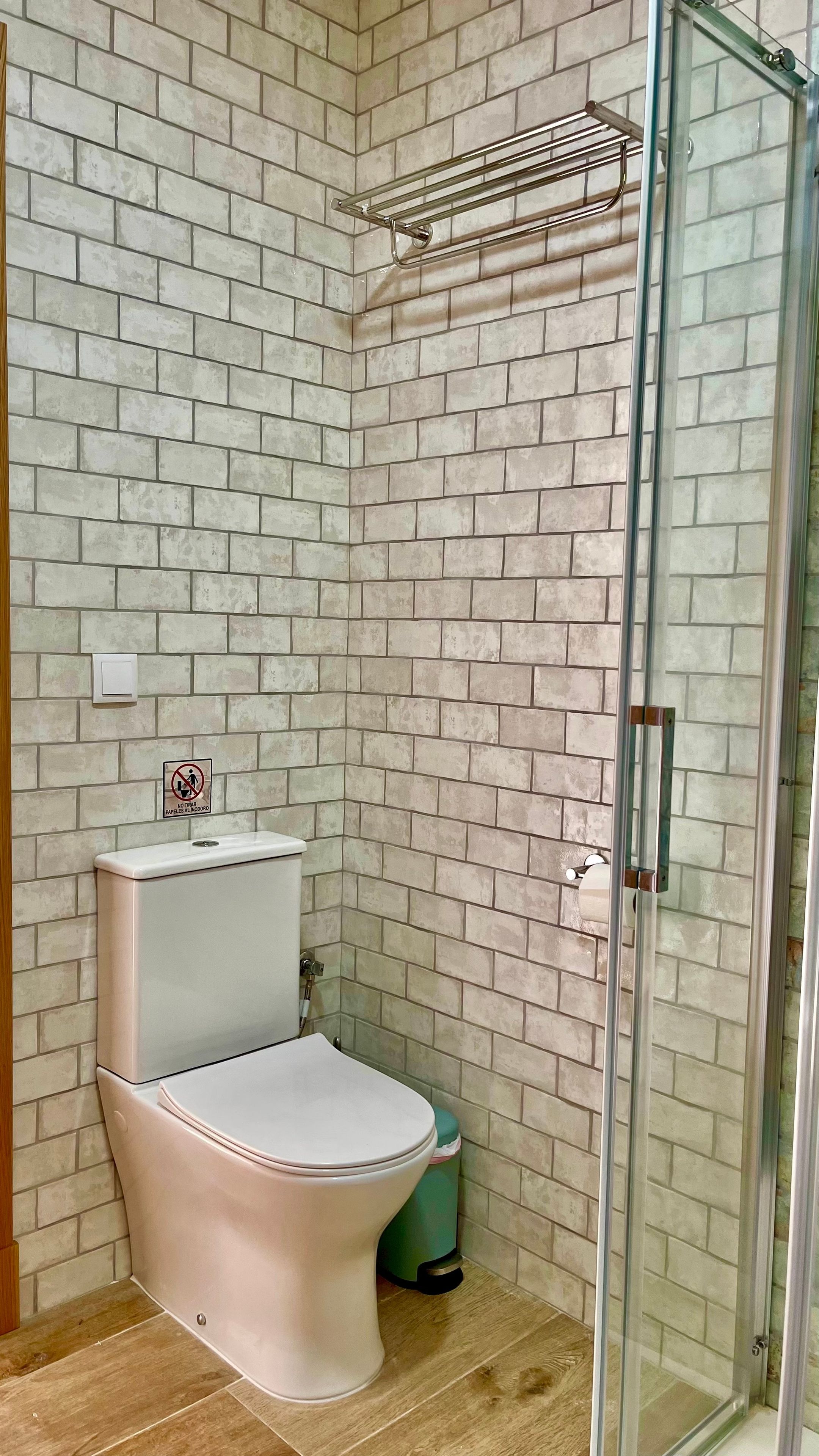 Un baño con inodoro, cabina de ducha de vidrio y pared con azulejos.