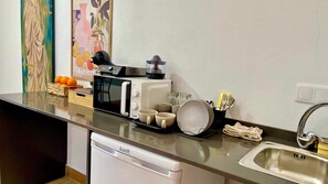 Una kitchenette con microondas, tostadora y hervidor. Hay tazas, una cesta de naranjas y un lavabo con grifo.