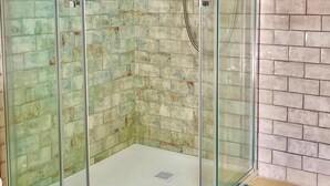 A glass-enclosed shower with a tiled wall, a metal shower head, and a drain. - Casa Golondrinas Verdes, Cartaya – Private Garden, Beach & Pets Welcome (Cartaya)