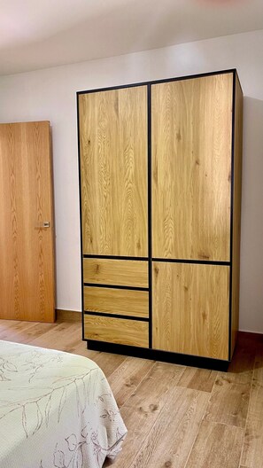 A room with a wooden wardrobe, a bed with a floral bedspread, and a wooden floor.