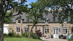 A stone building with a gabled roof, multiple windows, and a front porch with a bench. - Hill crest farmhouse (Vengeons)