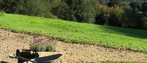 Um jardim com um carrinho de mão, uma pilha de folhas e vista para o campo.