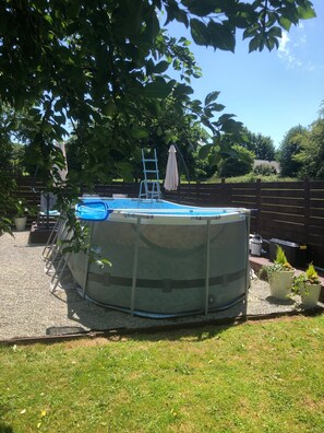 An above-ground swimming pool with a ladder and a covered area, surrounded by a wooden fence and potted plants. - Hill crest farmhouse (Vengeons)
