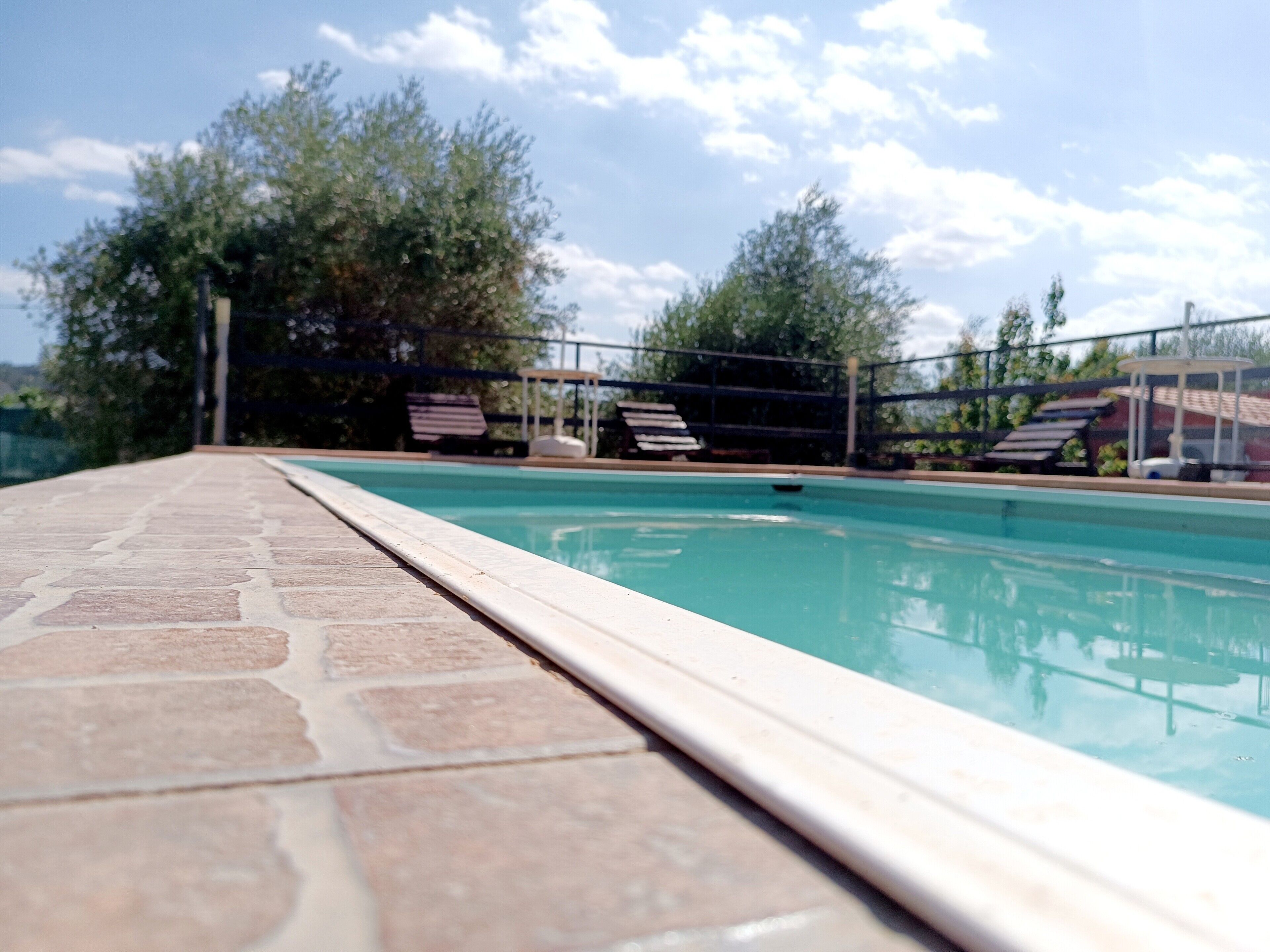 Ein Swimmingpool mit einer Fliesenkante, umgeben von Liegestühlen und einem Zaun.