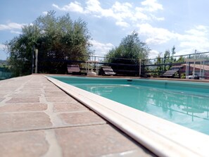 Ein Swimmingpool mit einer Fliesenkante, umgeben von Liegestühlen und einem Zaun.
