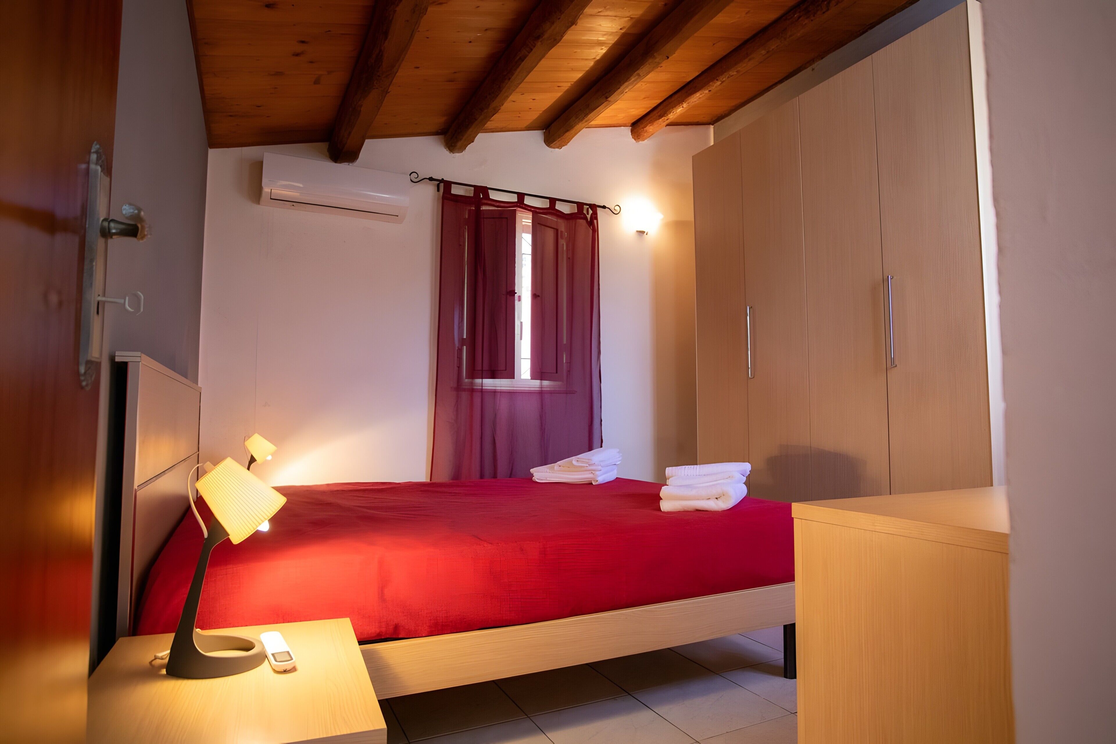 Une chambre à coucher avec un lit, une table de chevet avec une lampe, une armoire et une fenêtre avec des rideaux.
