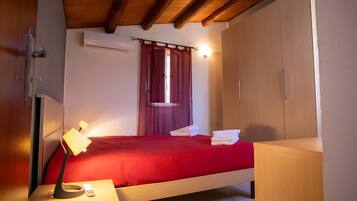 Une chambre à coucher avec un lit, une table de chevet avec une lampe, une armoire et une fenêtre avec des rideaux.