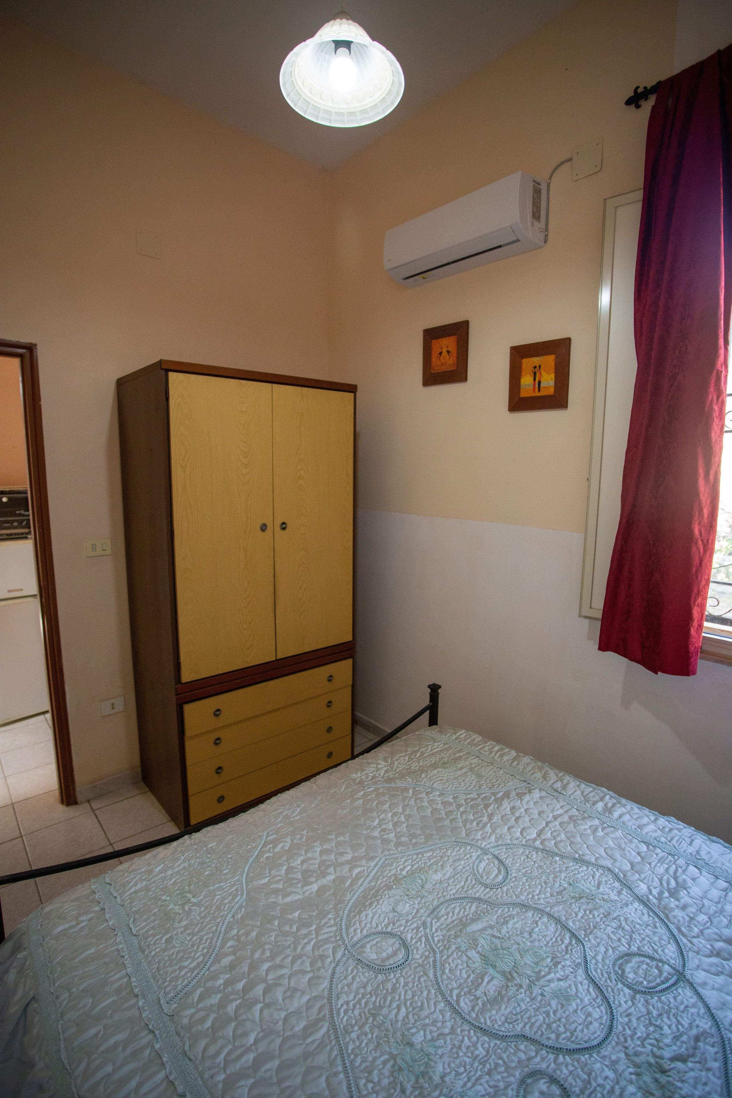 A bedroom with a bed, wardrobe, air conditioning unit, and two wall-mounted pictures.
