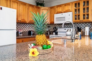 Eine Küche mit Holzschränken, einer Mikrowelle, einem Spülbecken und einer Obstschale mit einer Ananas, Limetten und einer gelben Blüte.
