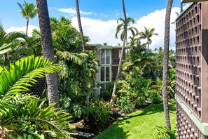 A tropical garden with palm trees, a building with a grid-like facade, and a well-maintained lawn. - 🏖️Top-Floor Kona Condo with A/C & Private Lanai (Kailua Kona)