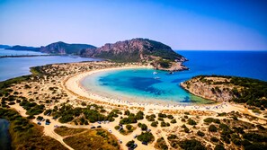 An aerial view of a coastal area with a beach, boats, and a mountainous backdrop.
