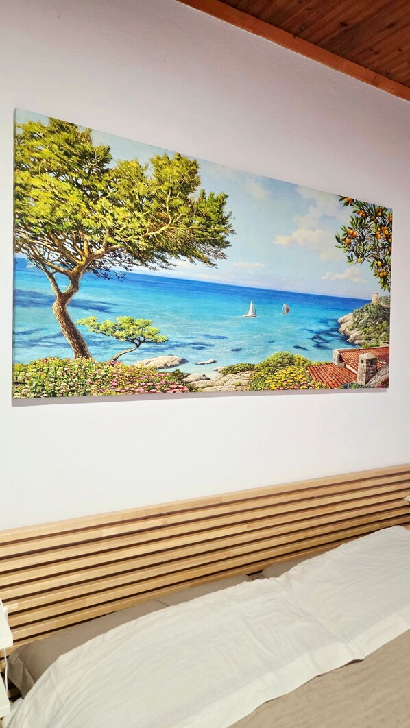 A bedroom with a bed, wooden slats, and a painting of a coastal landscape.