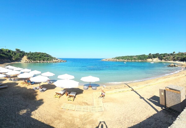 A beach with sun loungers and umbrellas, a clear sky, and calm sea.