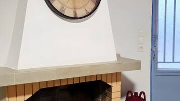 Una habitación con chimenea de ladrillo, un reloj de pared grande y un jarrón rojo.