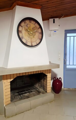 A room with a brick fireplace, a large wall clock, and a red vase.