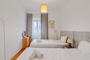 Hotellihuone, jossa on kaksi sänkyä, yöpöytä lampulla, puinen lipasto, peili ja ikkuna, jossa on verhot.