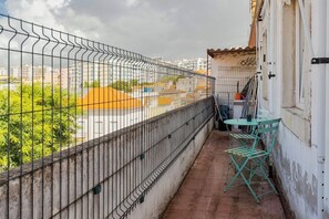 Ein Balkon mit Metallgeländer, einem kleinen Tisch mit Stühlen und Blick auf Gebäude im Hintergrund.