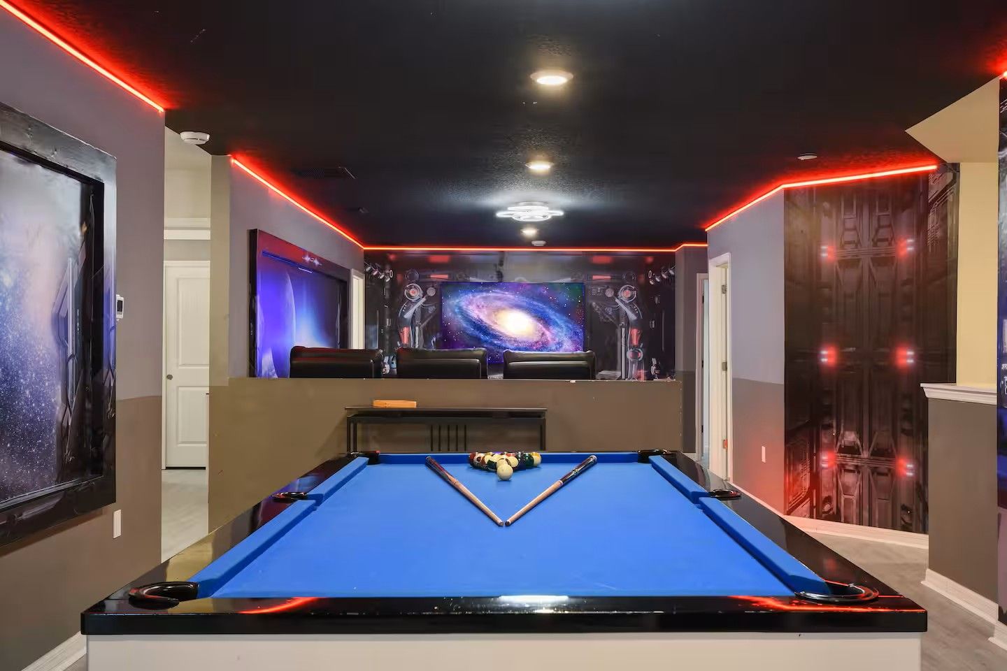 A pool table with a blue felt surface, surrounded by walls with space-themed artwork and red neon lighting.