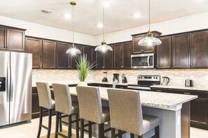 A modern kitchen with dark wood cabinets, stainless steel appliances, and a central island with bar stools. - Star Wars 10BR Villa | Pool, Theater & Games (Davenport)