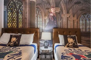 Een kamer met twee bedden, elk met een kussen waarop het gezicht van een personage is afgebeeld. Een tafel met een lamp staat tussen de bedden. De kamer heeft een gotische architectuur met boogvensters en een hoge plafond.