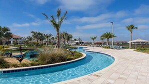 A swimming pool with a curved design, surrounded by palm trees and lounge chairs, set on a paved area with a clear sky above. - Storey Lake 8BR Family Adventure | Pool, Spa, Theater & Themed Rooms (Kissimmee)