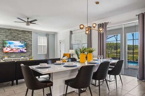 Un espace repas moderne doté d’un grand îlot central, de chaises noires et d’un téléviseur fixé au mur.