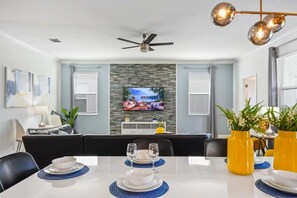 Een moderne eethoek met een flatscreen televisie aan een gestructureerde muur, een plafondventilator en een gedekte tafel met blauwe placemats.