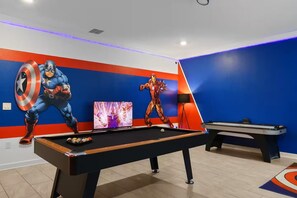 Ein Zimmer mit Billardtisch, Fernseher und zwei Wandmalereien von Superhelden.