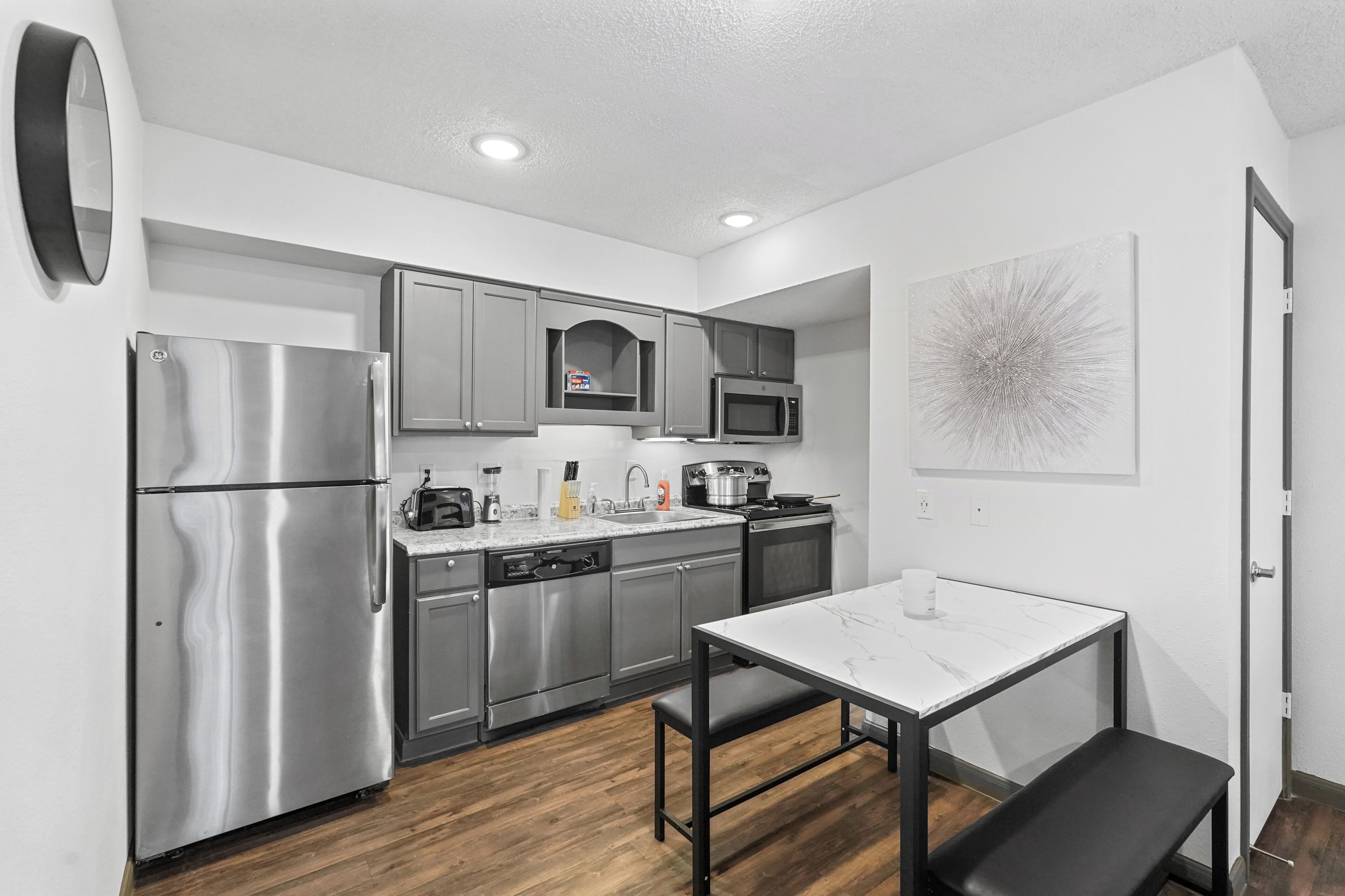 A modern kitchen with stainless steel appliances, a marble countertop, and a dining area with a bench.