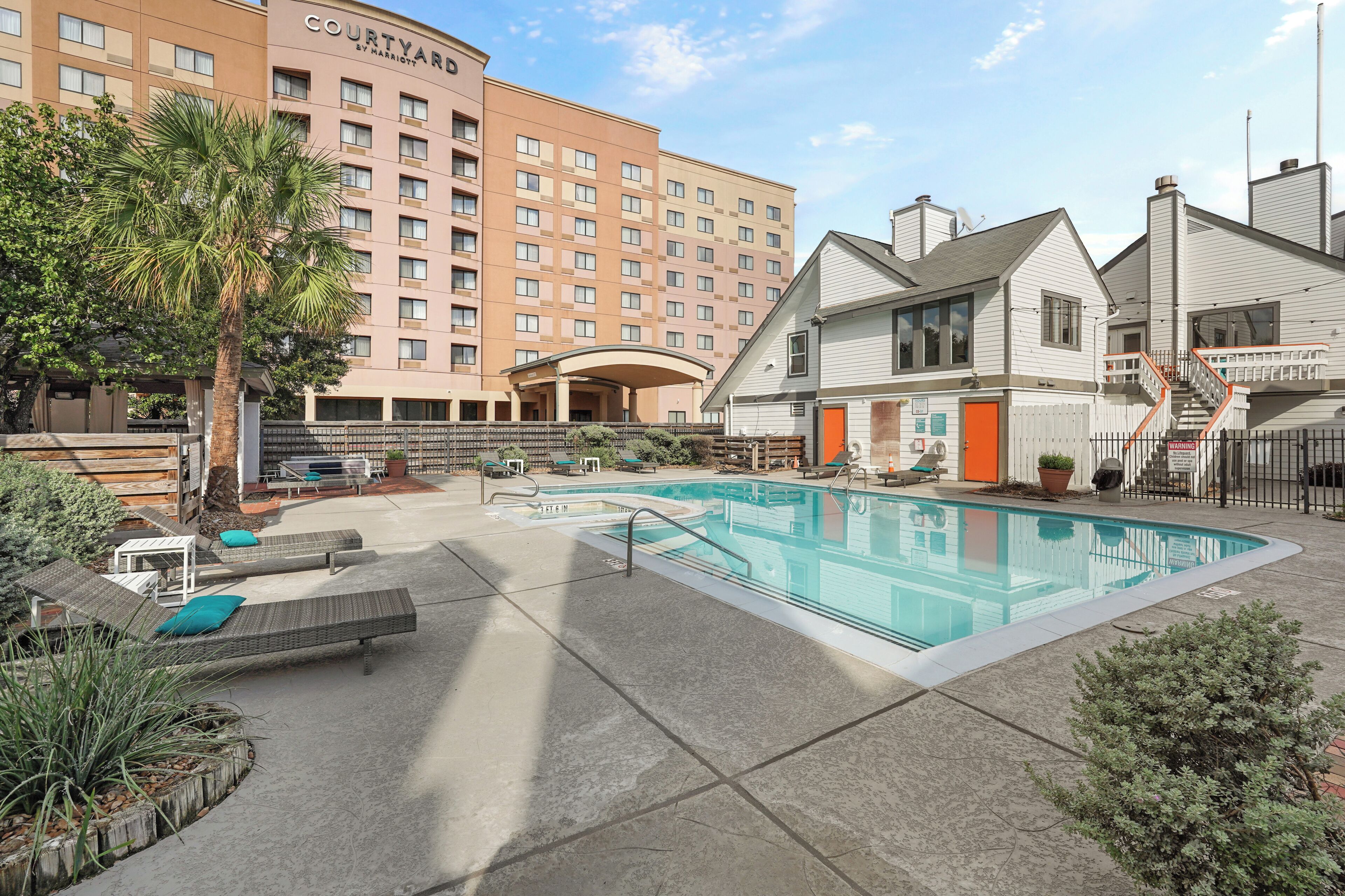 A hotel courtyard with a swimming pool, lounge chairs, and a large building in the background.