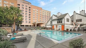 Un patio de hotel con piscina, sillas de descanso y un edificio grande al fondo.