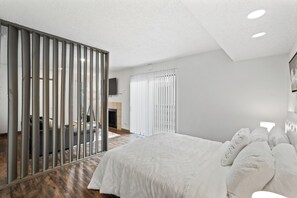 A modern bedroom with a large bed, a wooden floor, a sliding glass door, and a television on the wall. - Modern King Studio, Pool, Near MD Anderson and NRG (Houston)