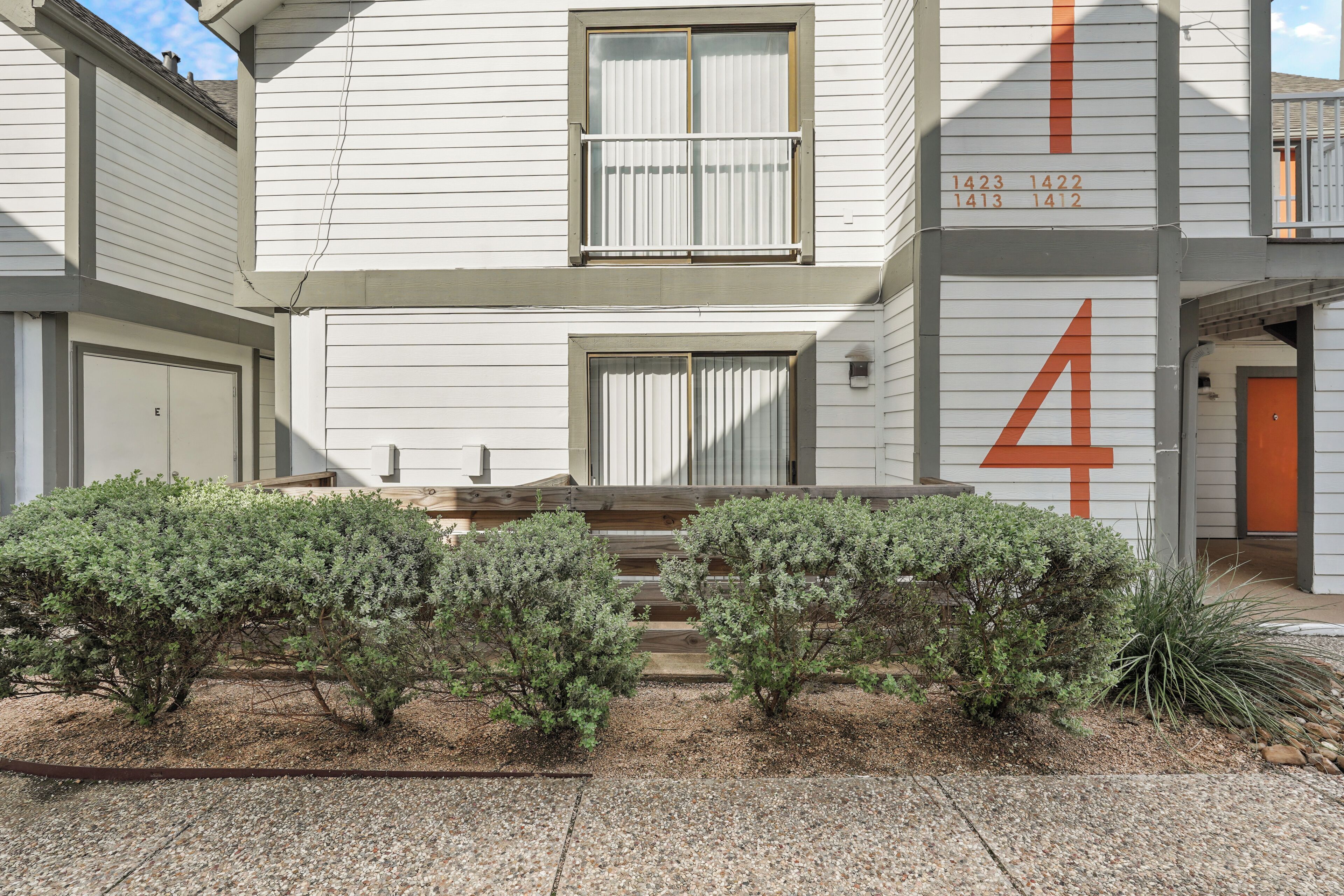 A two-story building with a number '4' on the side, a garage, and a small garden with shrubs.