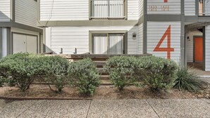 Un edificio de dos pisos con el número 4 en la fachada, un garaje y un pequeño jardín con arbustos.