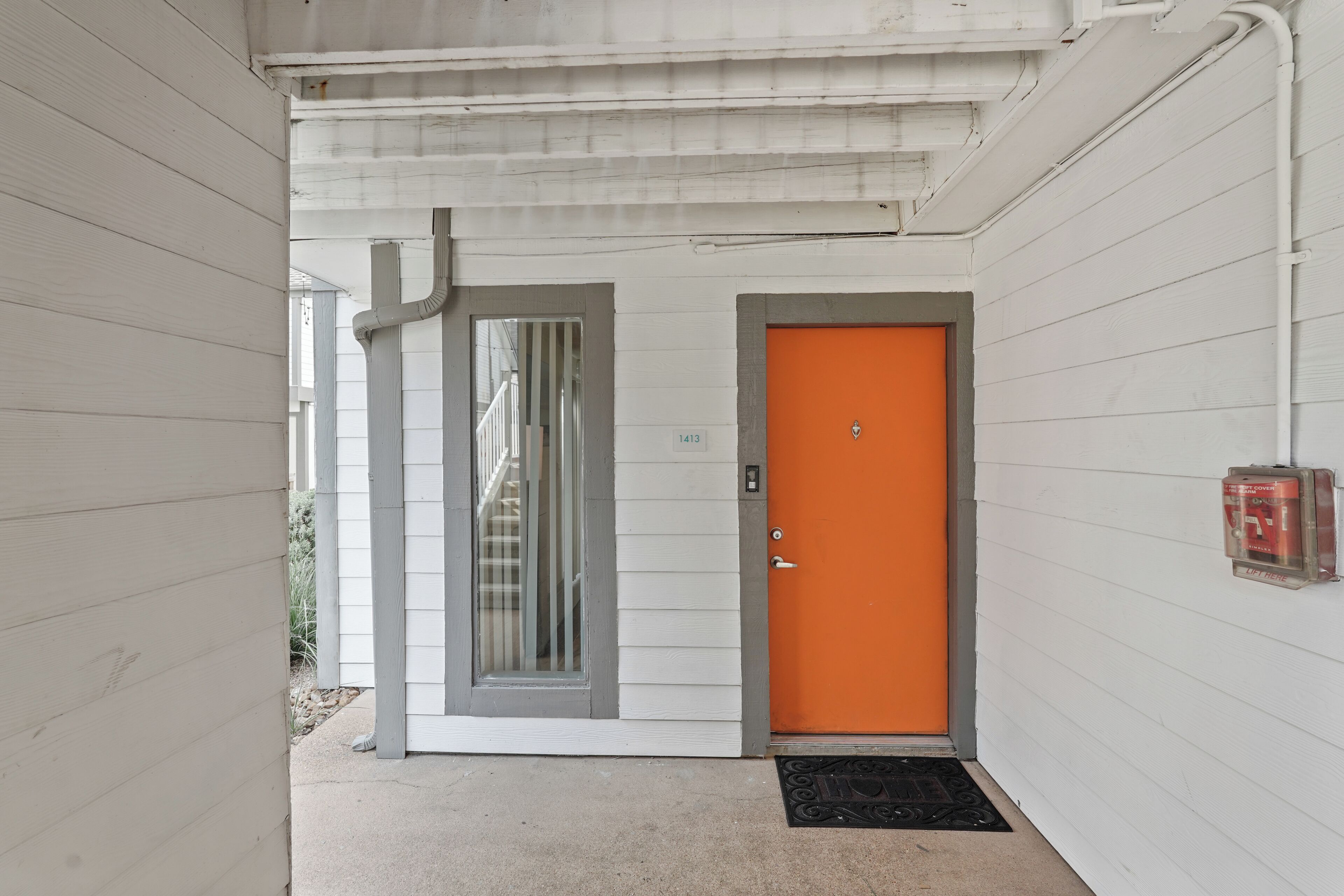 Ein weißes Gebäude mit einer grauen und einer leuchtend orangefarbenen Tür.