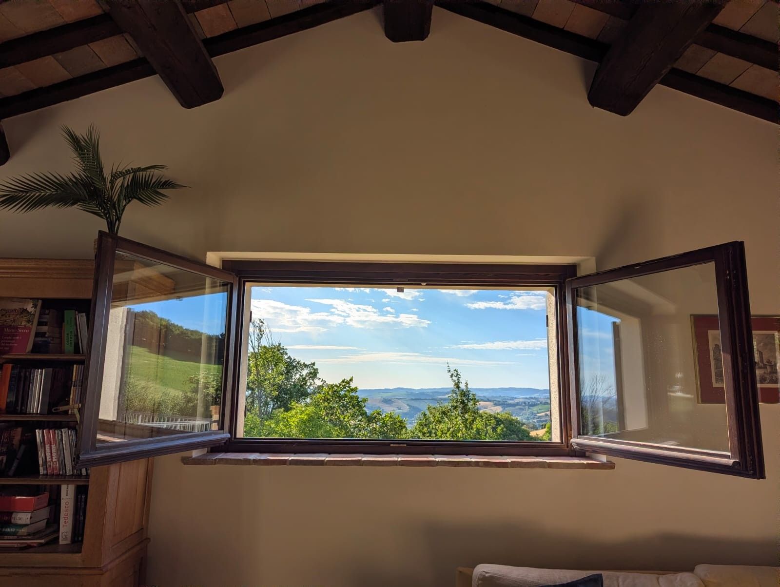 Ein Zimmer mit großem Fenster und Blick auf Grünflächen und Hügel.