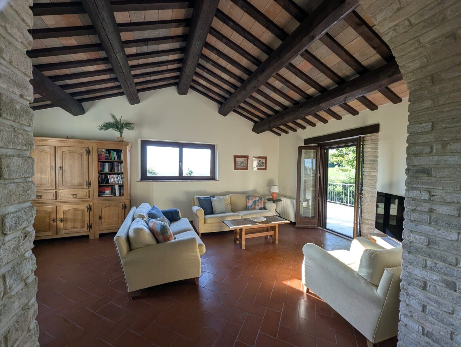 A spacious living area with a high ceiling, a fireplace, a large window, and a stone wall.