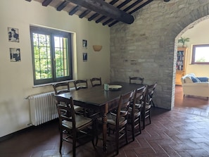 A dining area with a large wooden table and chairs, a window with a view of greenery, and a stone wall. - Holiday Home 'Alloro' with Mountain View, Private Pool and Wi-Fi (Pergola)
