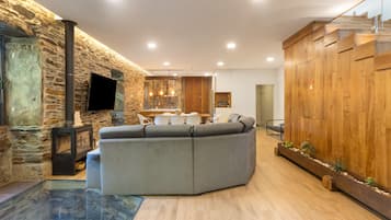 Un salon moderne avec un mur en pierre, un canapé d’angle, un téléviseur à écran plat et un escalier en bois.