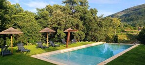 A swimming pool with lounge chairs and thatched umbrellas, surrounded by lush greenery and hills. - Country House 'Quinta Da Azenha' with Air Conditioning (Nespereira)