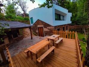 A modern house with a stone exterior, a wooden deck with benches, and a stone pathway leading to the entrance. - Country House 'Quinta Da Azenha' with Air Conditioning (Nespereira)