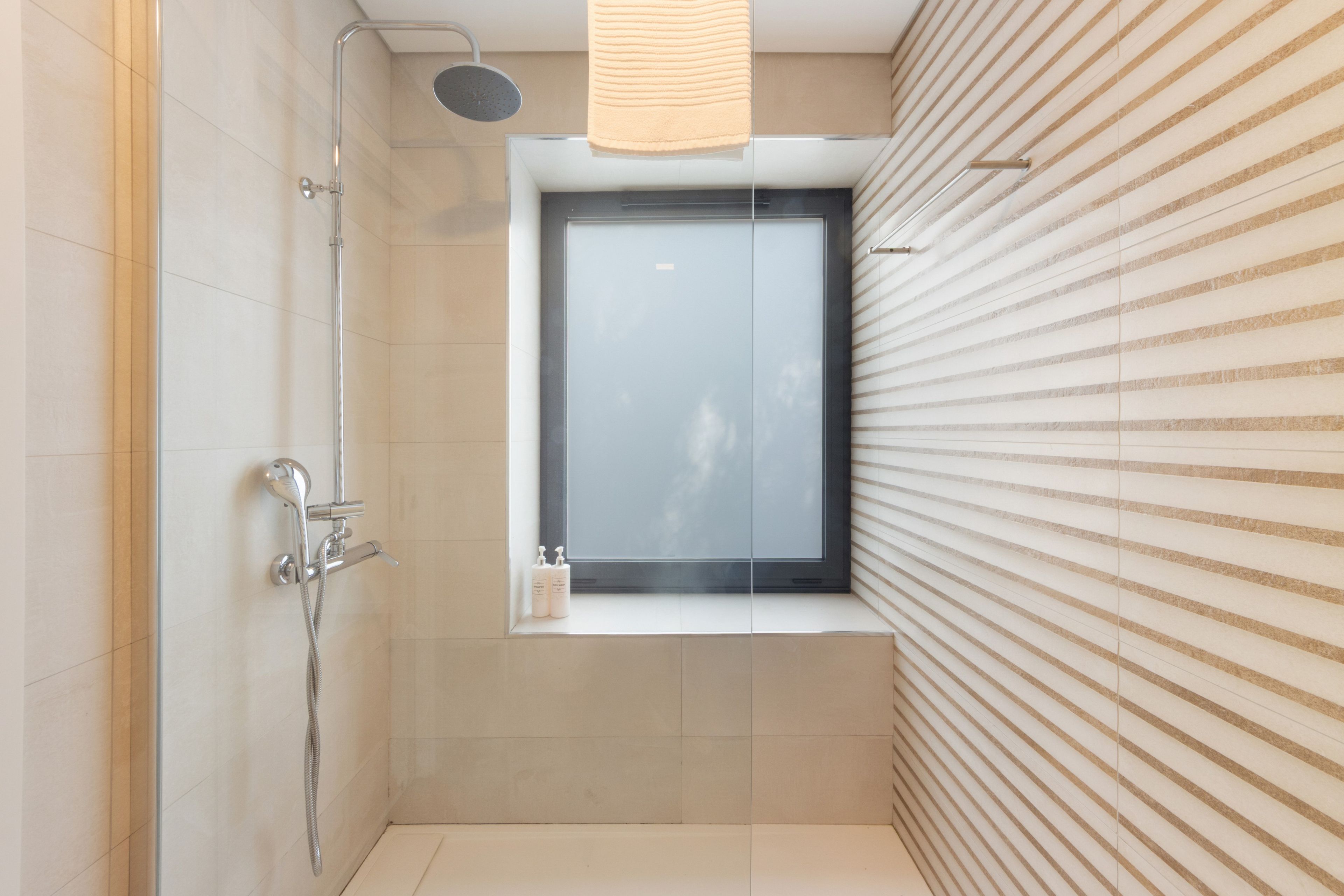 Une salle de bain moderne avec une douche, une fenêtre et une serviette accrochée au mur.