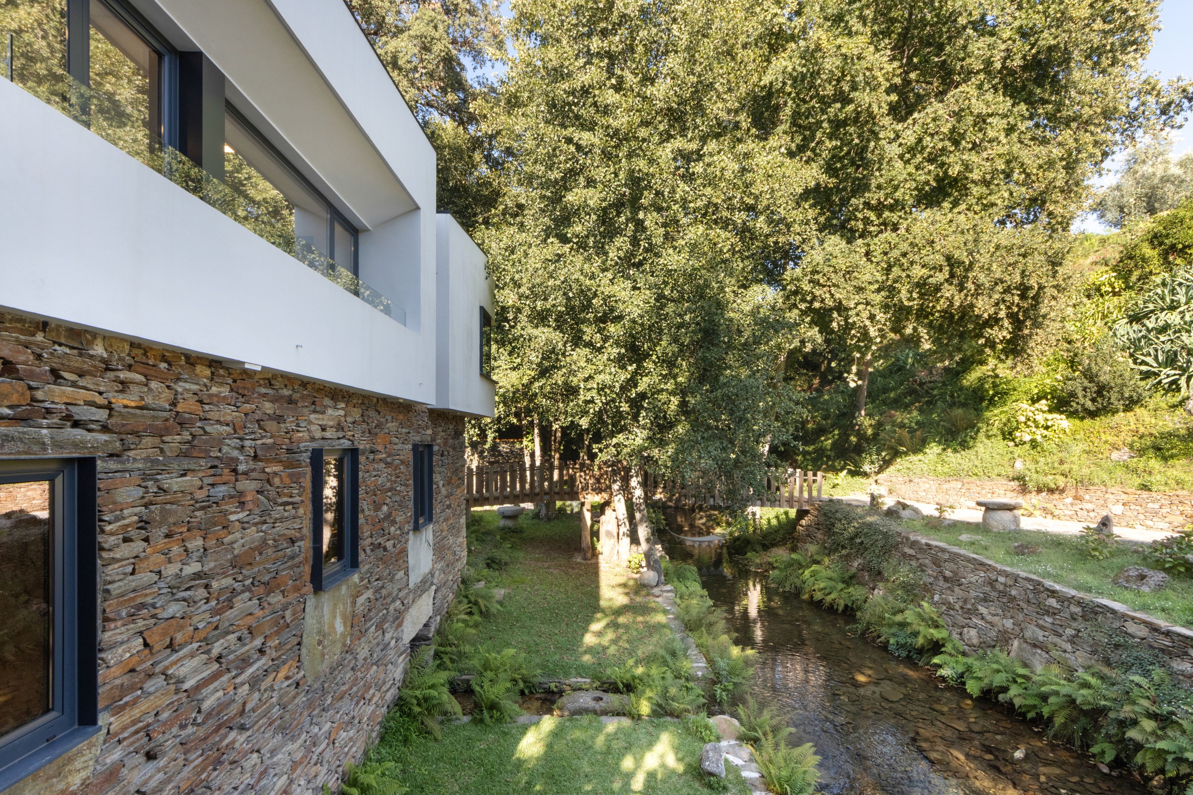 A modern building with a stone facade and a small stream running through a garden.