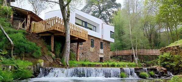 A modern building with a stone base, wooden balconies, and a waterfall in the foreground. - Country House 'Quinta Da Azenha' with Air Conditioning (Nespereira)